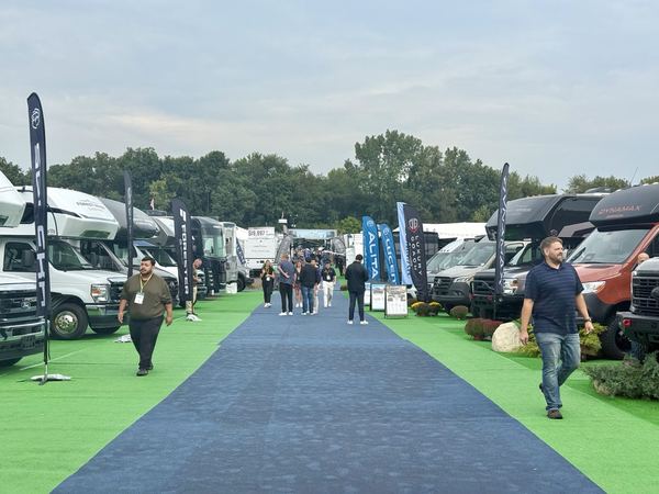 RVs and visitors beside a dark blue walkway and green carpet under an overcast sky at Forest River Open House