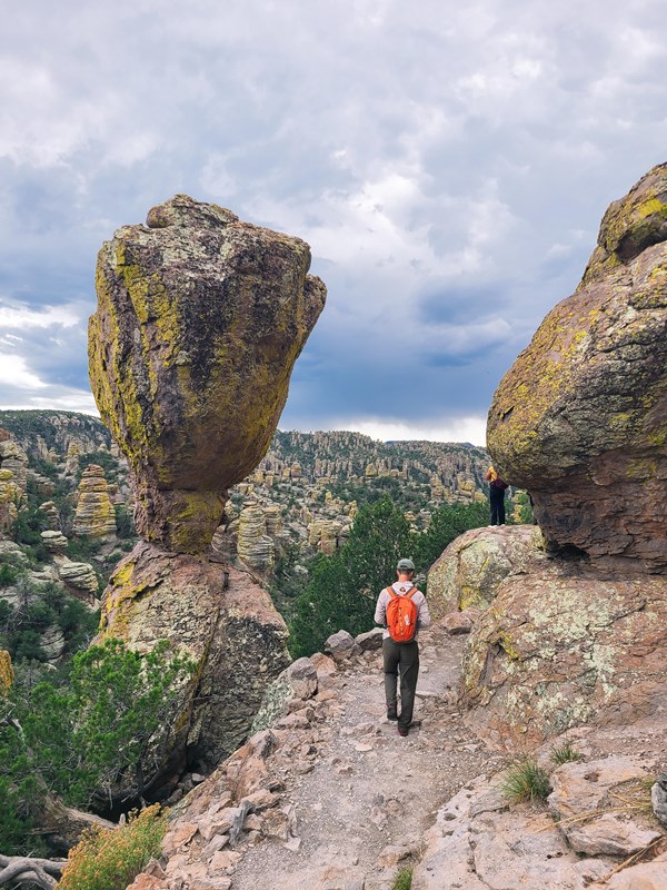 Hiker approaching a large balanced rock beside a trail in Chiricahua National Park